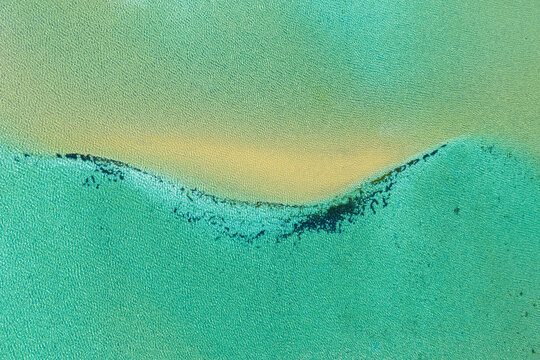 Aerial view of a crescent-shaped sandbar surrounded by vibrant turquoise water and patches of dark seaweed in Australia.