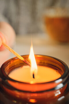 Hand lighting soy candle in glass jar, creating warm cozy atmosphere