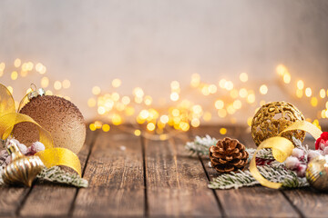 Naklejka premium A Christmas background featuring warm gold baubles, a glittering snowflake, star, and pinecone arranged on rustic wood, set against a soft backdrop with twinkling lights and copy space.