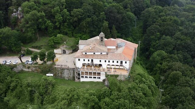 Aerial view of Mare de deu de la salut Hermitage, dramatically perched on a rocky cliff above dense forests, overlooking the beautiful mountain landscapes of Girona, Catalonia. 