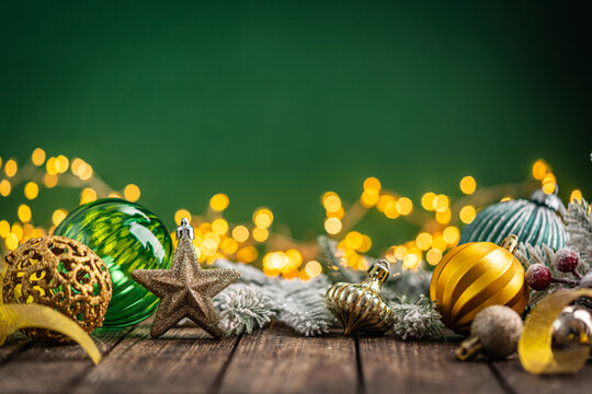 A Christmas background featuring gold and emerald ornaments, a glittering star, and frosted pine on rustic wood, set against a rich green backdrop with twinkling lights and copy space.