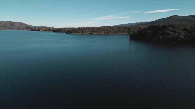 Aerial glide above a tranquil reservoir bordered by rolling hills