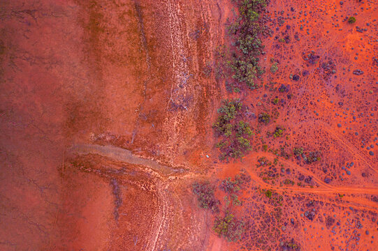Aerial view of the arid Australian outback, showcasing vibrant red earth, sparse scrub vegetation, and intricate patterns of dry creek beds and dirt tracks in Australia.