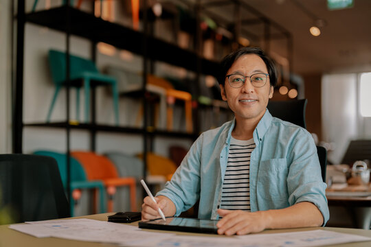 Happy Asian freelancer relaxing comfortably with hands behind head at modern coworking desk, demonstrating career satisfaction, employee wellbeing, contented productivity, work-life balance, and freed