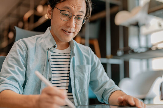 Happy Asian freelancer relaxing comfortably with hands behind head at modern coworking desk, demonstrating career satisfaction, employee wellbeing, contented productivity, work-life balance, and freed