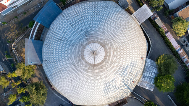 Aerial view of the large circular dome of a mosque with a geometric pattern, surrounded by trees and urban infrastructure in Boyolali, Central Java, Indonesia.