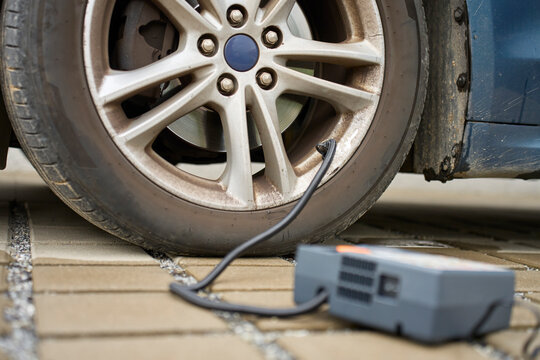 Portable tire inflator connected to car wheel and pumping air into tire