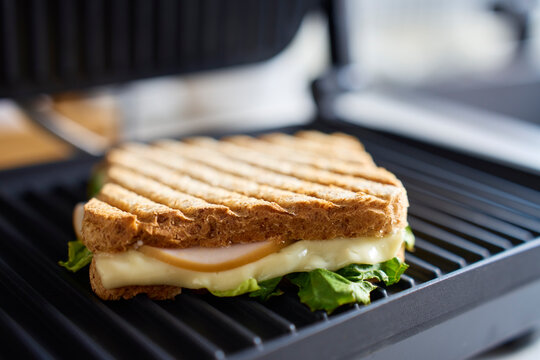 Sandwich with cheese, deli meat and lettuce cooking on electric grill