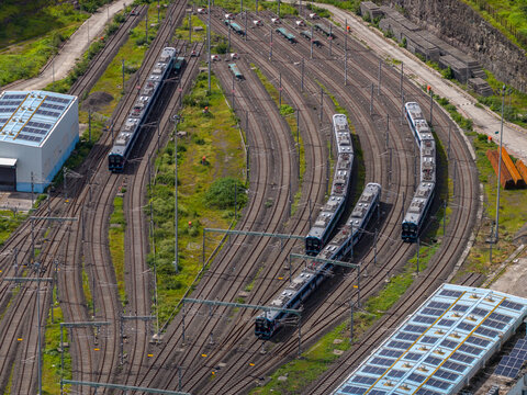 Aerial view of a railway yard with multiple passenger trains parked on parallel tracks, surrounded by greenery and industrial buildings with solar panels in Pune, Maharashtra, India.