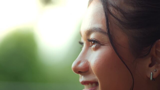Close up side profile of young Asian woman looking into distance with gentle smile in natural sunlight, detailed female eye and face portrait, vision