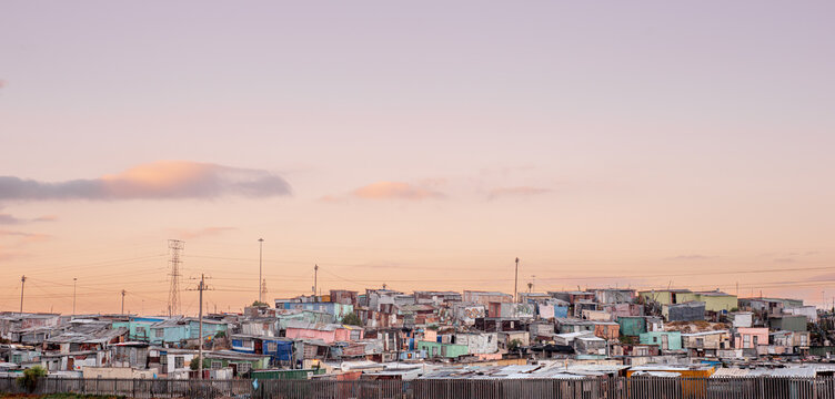 View of a township with colorful makeshift houses, power lines, and a soft sunset sky in South Africa.