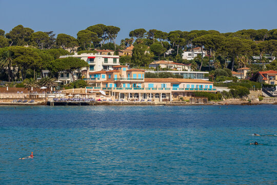 Mediterranean coastline at La Garoupe on Cap d'Antibes, featuring elegant villas, pine trees, beach club and swimmers in clear blue water