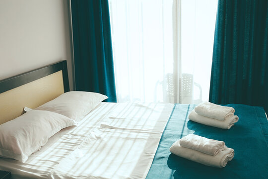 Bright bedroom with white bed linens and neatly folded towels on a blue bedspread
