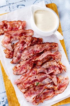 creamy sauce with bacon, in a sauce pan, on a wooden chopping board, next to fried bacon, top view