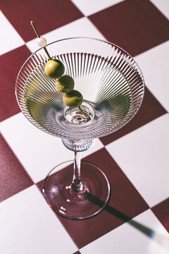 A martini glass with green olives, on a chessboard-style table, in the evening, vintage, retro, no people