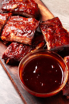 BBQ ribs with sauce served on a wooden board in a kitchen setting