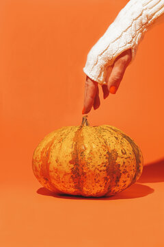 Hand reaches for a pumpkin on a bright orange background during autumn harvest season