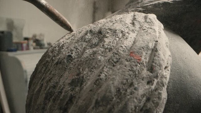 Sculptor uses pneumatic chisel on stone in artist workshop showing rough surface and fine stone dust during the carving process