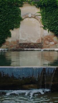Vertical video: Showing arch wall and pool developing ripples in yard, thin sheet forming over lip