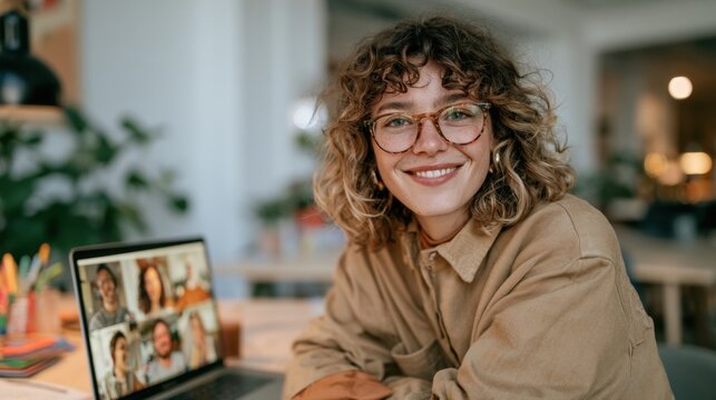 Woman smiles at the camera while sitting at a desk during a virtual meeting in a well-lit room