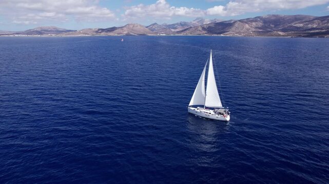 Sailboat with full mainsail and jib travels across the Mediterranean Sea near Naxos in the Cyclades Islands in daylight