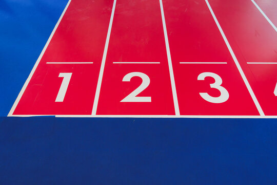 Red indoor running track lanes marked with white numbers and lines beside a blue sports surface.