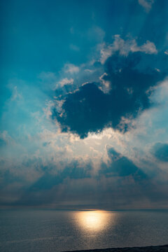 View of a dramatic sunset over the sea with sun rays breaking through dark clouds above the horizon in Doha, Doha Municipality, Qatar.