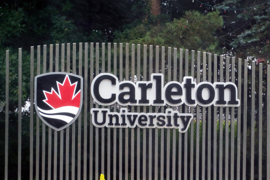 Ottawa, ON, Canada - Sept 14, 2026: Carleton University entrance sign and crest mounted on a metal fence with trees in the background.