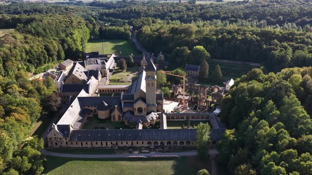 Aerial view of Orval Abbey surrounded by dense green forest on a bright sunny day