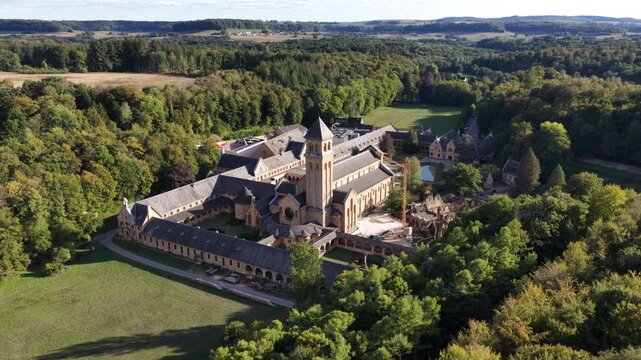 Aerial view of Orval Abbey surrounded by green forests on a bright sunny afternoon
