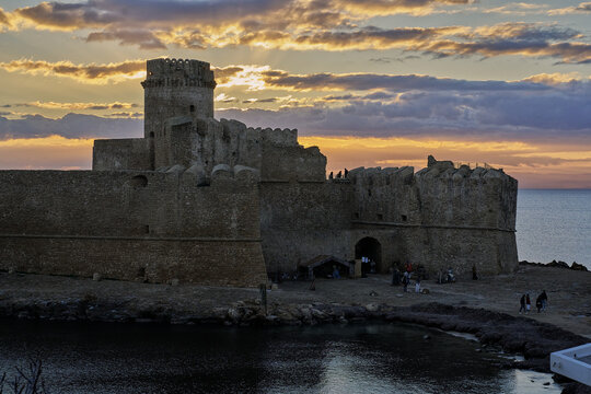 View of the historic Le Castella fortress at sunset with golden light reflecting on the stone walls and the sea in Calabria, Italy.