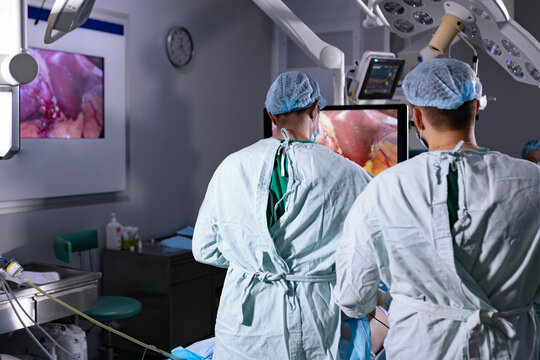 Surgeons look at monitor during laparoscopic operation. Two surgeons in sterile gowns and masks watch laparoscopic monitor during minimally invasive surgery