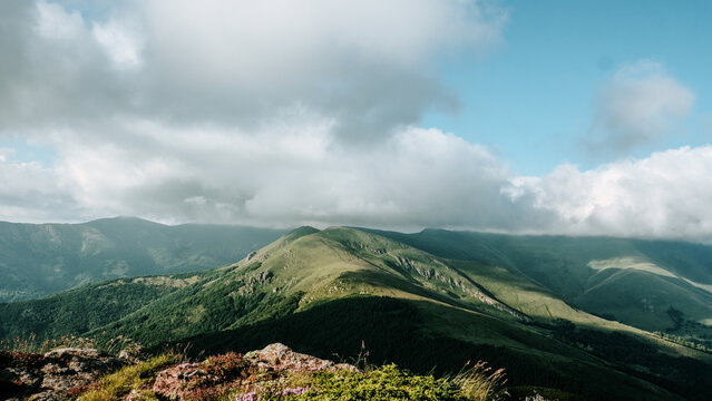 View of Stara planina mountain range with lush green slopes, rocky foreground, and clouds in a blue sky in Zaskovci, Pirot District, Serbia.
