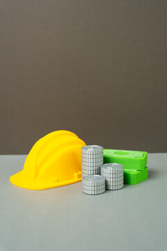 A yellow hard hat and cash money with coins. Concept of construction industry earnings and worker wages. Symbol of profitable building projects and pay. Skilled labor.
