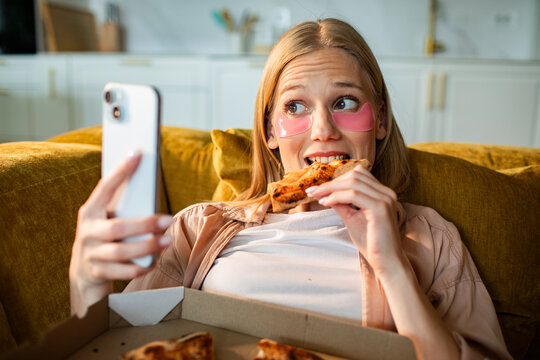 Young woman taking selfie while eating pizza at home