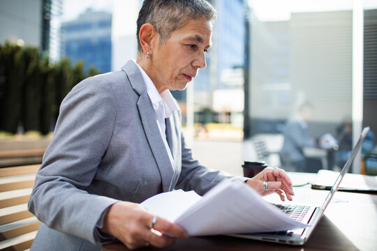 Mature businesswoman reviewing documents on laptop outdoors