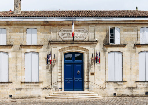Historic town hall with French flags, limestone facade and blue entrance door in Saint Emilion, Nouvelle-Aquitaine, France