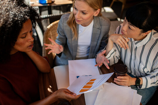 Three businesswomen reviewing charts at cafe table