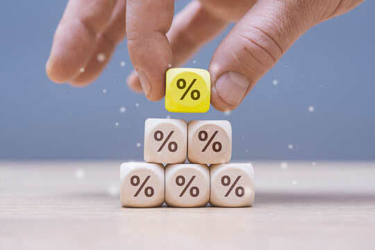 Percentage discount concept with hand placing a yellow percent block on a stack of wooden cubes. Finance, pricing strategy, savings and promotional advertising for business marketing.