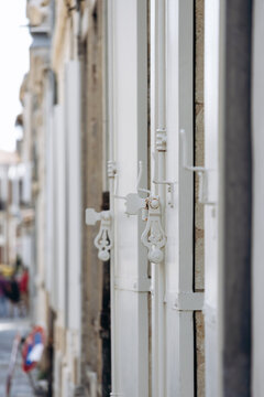Traditional white wooden shutters with decorative metal latches and hardware on a historic facade in Libourne, Nouvelle-Aquitaine, France.