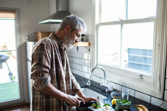 Mature man chopping fresh vegetables in home kitchen