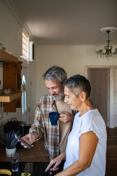 Happy senior couple using smartphone in home kitchen