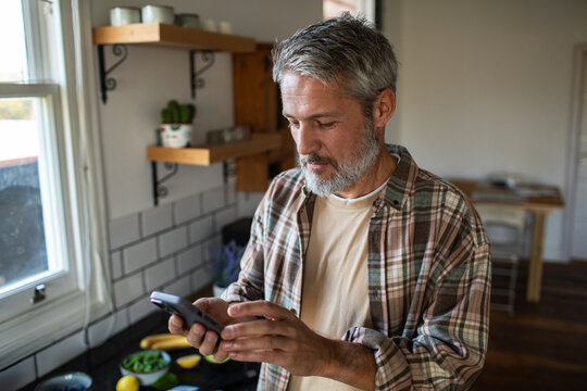 Mature man using smartphone in home kitchen
