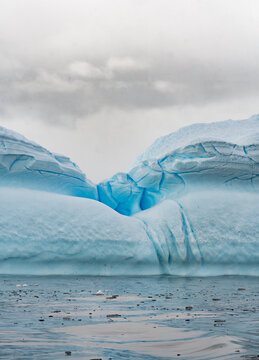 View of a massive blue iceberg floating in the cold waters of the Southern Ocean under a cloudy sky, Antarctica.