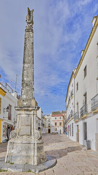View of a stone obelisk monument in a historic square surrounded by white buildings in Andalusia, Spain.