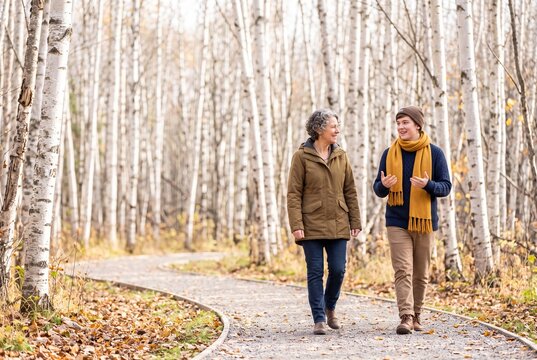 A mature mother and her adult son walk along a pathway through a birch forest, talking and enjoying an autumn day outdoors