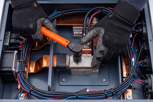 Electrician wearing protective safety gloves using an insulated torque wrench to tighten copper busbar connections in an industrial electrical panel