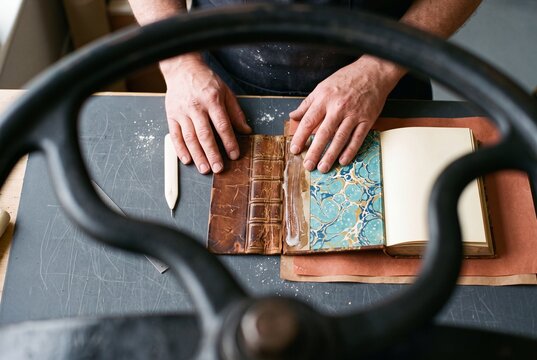 Professional bookbinder carefully restoring an antique leather book with glue and marbled endpaper in a workshop