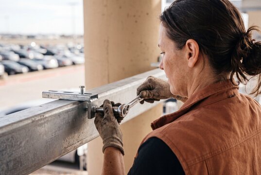 Female construction worker tightening a bolt on a steel structure with a ratchet wrench