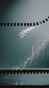 Vertical video: Rippling wave starting left bending glitter band on box over perforated film strip